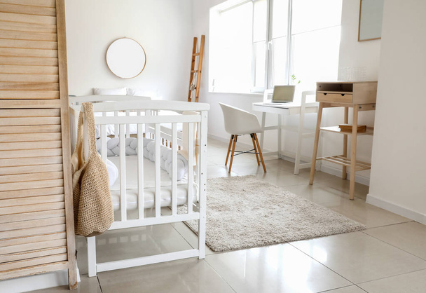Interior of light bedroom with white crib and modern workplace - Photo, Image