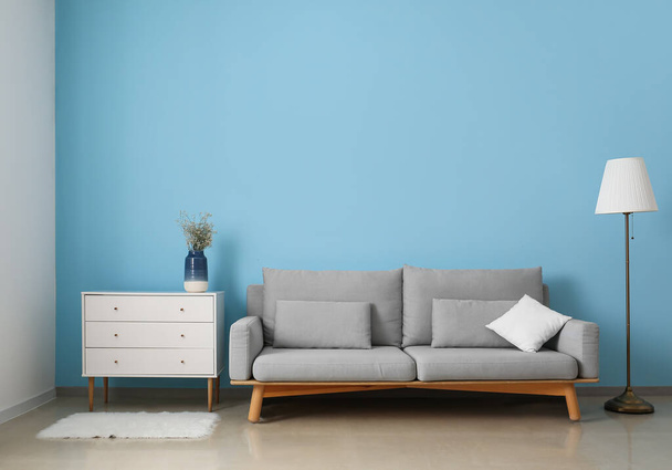 Szara sofa, komoda i lampa w pobliżu niebieskiej ściany - Zdjęcie, obraz