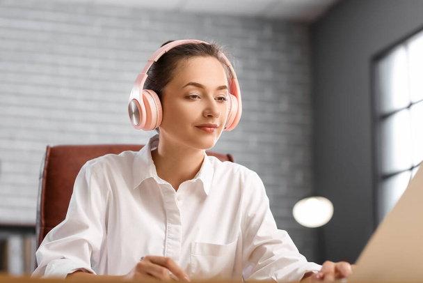 Όμορφη νεαρή γυναίκα που ακούει μουσική ενώ εργάζεται στο γραφείο - Φωτογραφία, εικόνα