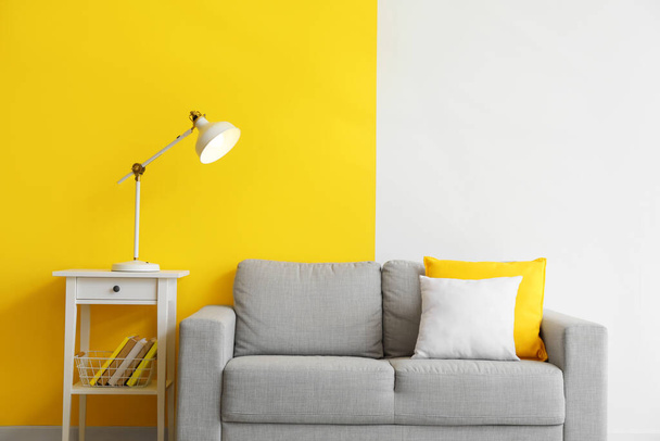 Mesa con lámpara brillante y sofá gris cerca de la pared de color - Foto, imagen