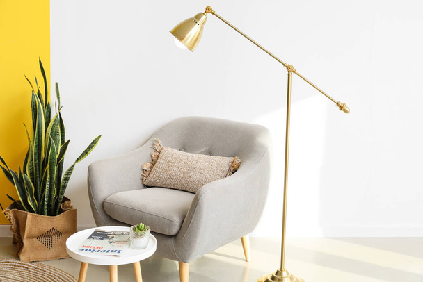 Golden standing lamp, armchair and table near light wall - Photo, Image