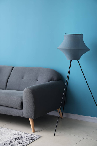 Stylish standard lamp and sofa near blue wall - 写真・画像