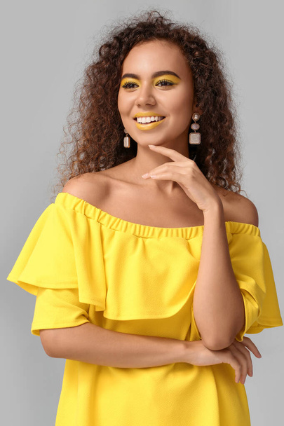 Beautiful African-American woman with makeup in yellow tones on grey background - Photo, Image
