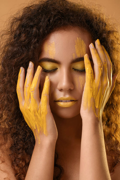 Beautiful young woman with yellow paint on her face and body against color background - Фото, зображення