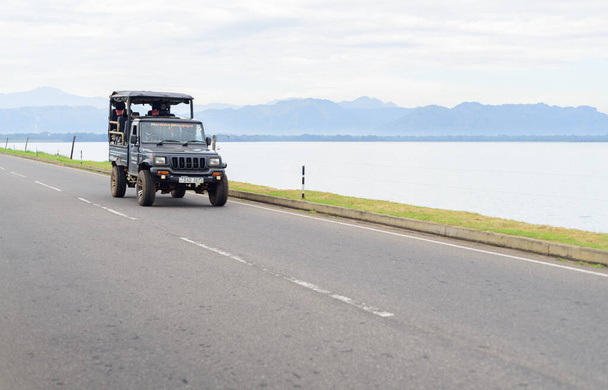 Udawalawa, Sri Lanka -12 12 2021 : Jeep safari sur route dans le barrage d'Udawalawe. Beau lac et la chaîne de montagnes brumeuses en arrière-plan. - Photo, image