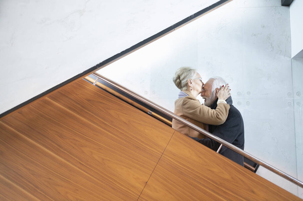 Elderly woman kissing her partner in a stairway - Фото, изображение