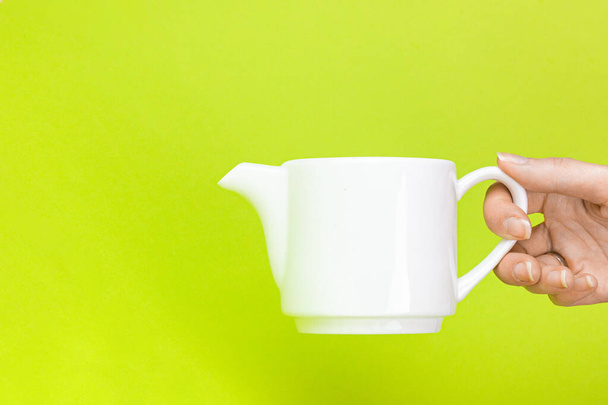 Nainen käsi pitämällä vedenkeitin teekannu vihreällä taustalla. Panimo- ja juomatee. - Valokuva, kuva