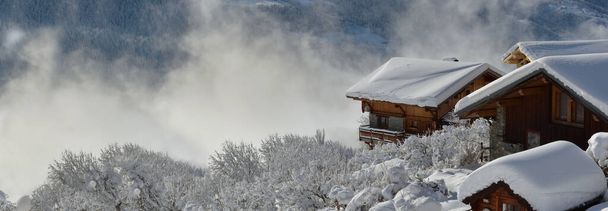 Holzchalets in Alpendorf mit Schnee bedeckt mit Blick auf bewölkte Tallandschaft - Foto, Bild