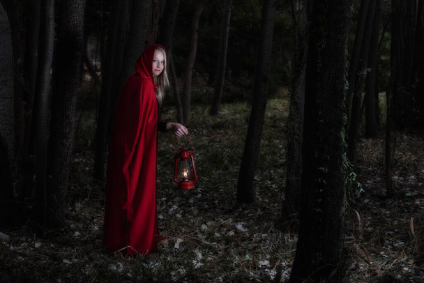 Приваблива жінка одягнена в червону прогулянку в темному лісі з ліхтарем
 - Фото, зображення