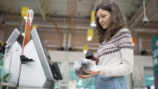 Een jonge vrouw bij de self-service kassa in een supermarkt doet aankopen - Video