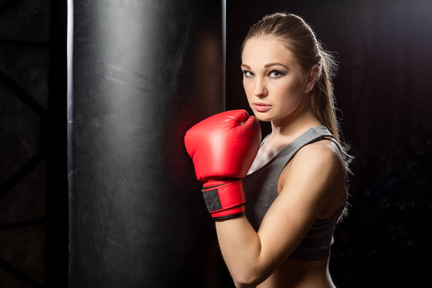 Young woman near the punching bag on a dark background. - Foto, Bild