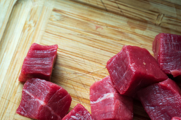 cubes of sliced raw roast beef meat on wooden cutting board closeup - Zdjęcie, obraz
