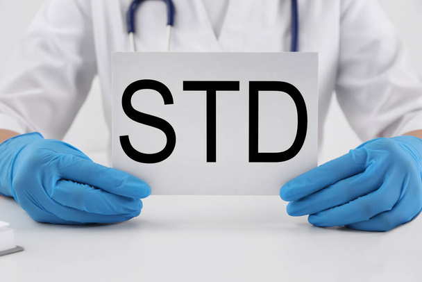 Doctor holding sheet of paper with abbreviation STD at white table, closeup - Photo, image