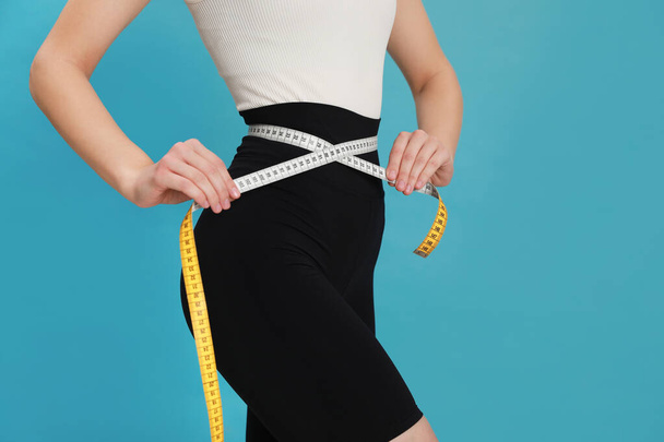 Woman in sportswear measuring waist with tape on light blue background, closeup. Space for text - Foto, Imagem