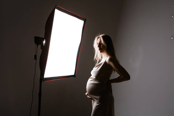 a pregnant woman in a black suit strokes her belly on a white background. A girl in the studio in the spotlight. professional lighting. - Valokuva, kuva