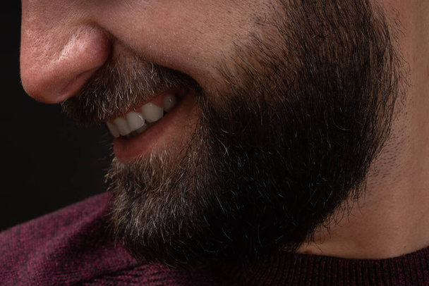 close-up portrait in profile of young smiling, happy man with thick black beard and mustache on black background - Zdjęcie, obraz