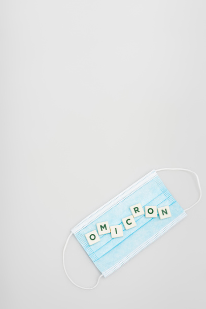 top view of medical mask and white cubes with omicron lettering on grey background with copy space - Fotó, kép