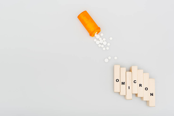 top view of pills and wooden bricks with omicron lettering on grey background - Фото, изображение