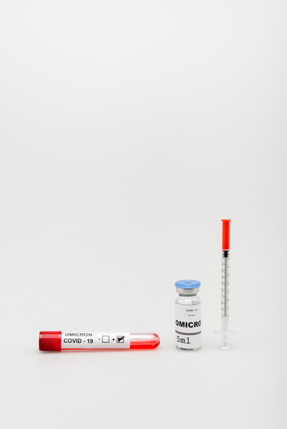 test tube with positive result near covid-19 omicron variant vaccine and syringe on grey background - Foto, Bild