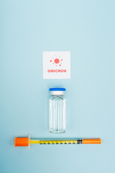 top view of white card with omicron lettering and bacteria near vaccine vial and syringe on blue - Foto, Bild