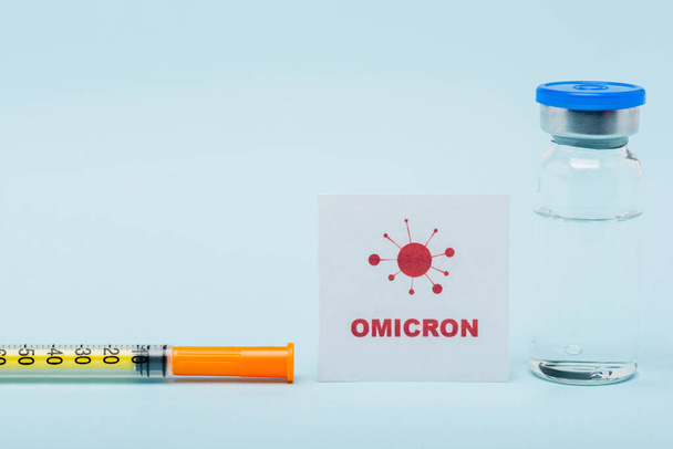card with omicron lettering near syringe and vaccine vial on blue background - Photo, image