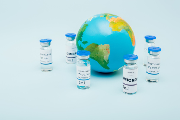 covid-19 omicron variant vaccine bottles near globe on blue background - Foto, afbeelding