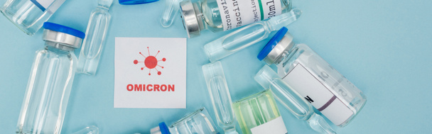 top view of card with red omicron lettering and bacteria icon near vaccine bottles and ampoules on blue, banner - Zdjęcie, obraz