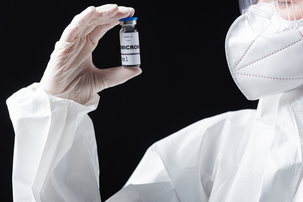 частковий вигляд лікаря в медичній масці та костюмі з маскою, що тримає вакцину проти омікрону в костюмі ковадла-19 ізольовану на чорному
 - Фото, зображення
