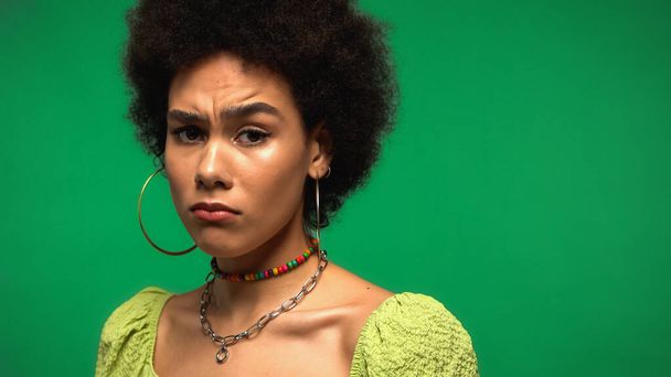 sad african american woman frowning and looking at camera isolated on green - Photo, Image