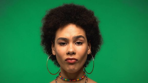 Sceptische Afro-Amerikaanse vrouw op zoek naar camera geïsoleerd op groen - Foto, afbeelding