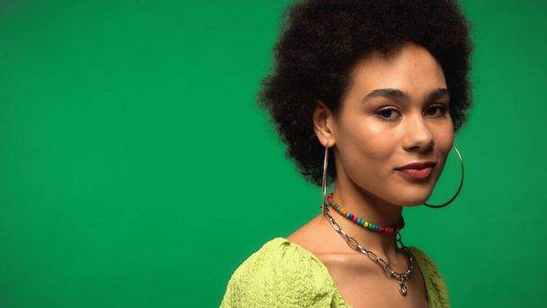 african american woman in hoop earrings looking at camera isolated on green  - Foto, afbeelding