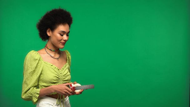 pleased african american woman holding headphones isolated on green - Foto, Imagen