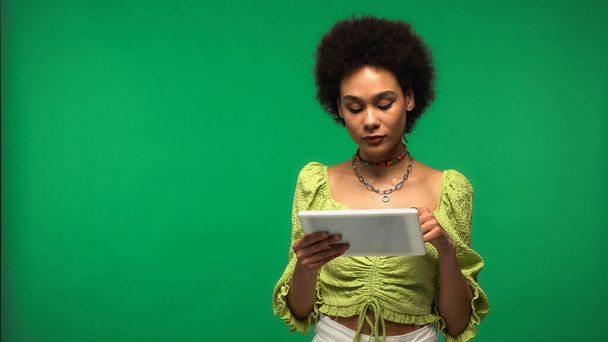 mulher americana africana encaracolado em blusa usando tablet digital isolado em verde  - Foto, Imagem