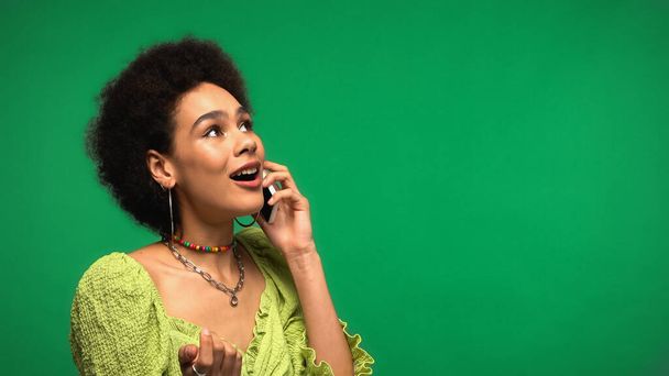 amazed african american woman in blouse talking on smartphone isolated on green  - Foto, Imagen