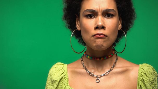 angry african american woman in hoop earrings looking at camera isolated on green - Foto, Imagen
