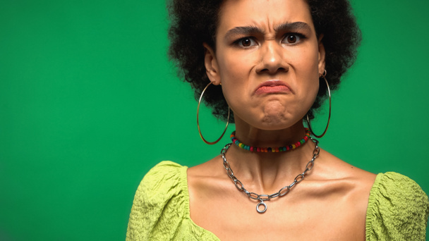 angry african american woman in hoop earrings grimacing isolated on green - Foto, Imagen