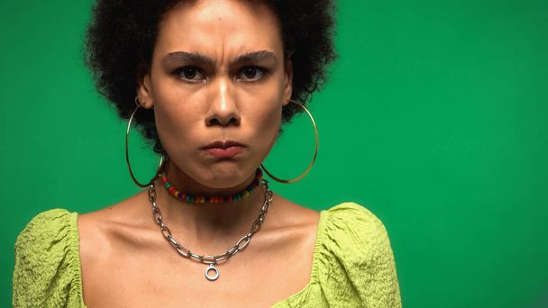 upset african american woman in hoop earrings looking at camera isolated on green - Photo, Image