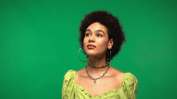 dreamy african american woman in hoop earrings looking away isolated on green - Photo, Image