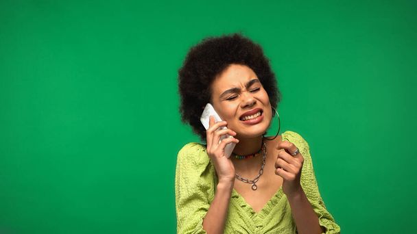 benadrukte Afrikaans-Amerikaanse vrouw in blouse praten op mobiele telefoon geïsoleerd op groen - Foto, afbeelding
