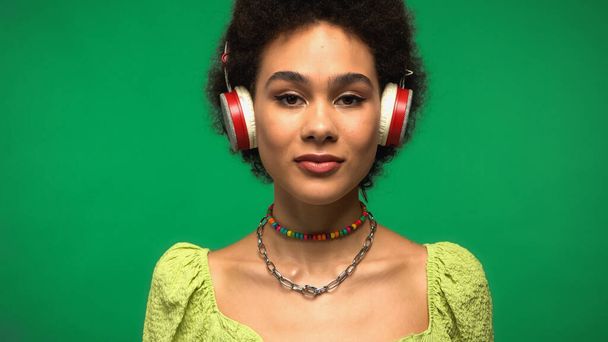 junge afrikanisch-amerikanische Frau mit drahtlosen Kopfhörern, die isoliert auf grün Musik hört  - Foto, Bild