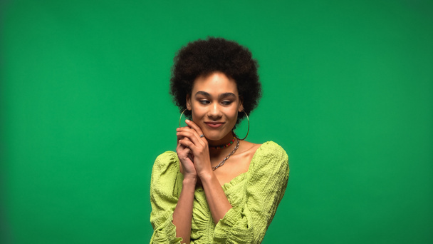 smiling african american woman in blouse and hoop earrings looking away isolated on green  - Foto, Imagem