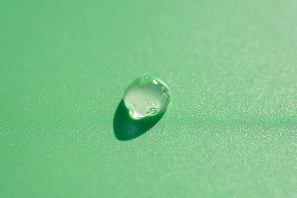 Gota transparente de gel de suero del producto cosmético. Textura líquida con burbujas sobre fondo verde en vista superior - Foto, imagen