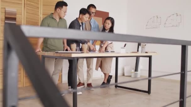 Team di architetti asiatici professionisti che discutono piano di costruzione steso sulla scrivania presso l'ufficio moderno - Filmati, video