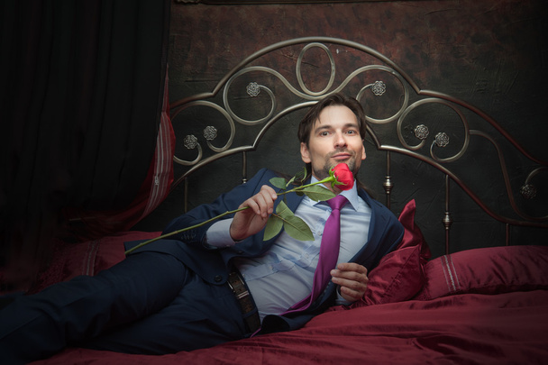 Smiling businessman lying on bed with flower - Fotó, kép