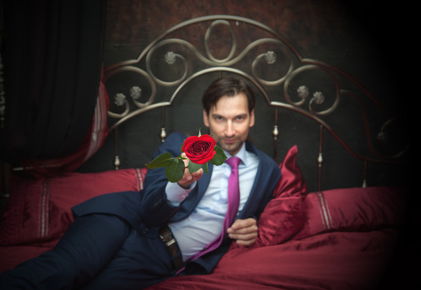 Smiling businessman lying on bed with flower - Foto, Bild