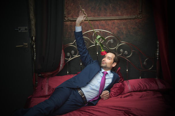 Smiling businessman lying on bed with flower - Foto, Bild