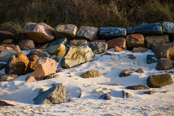 Μεγάλες πέτρες καλύπτουν την παραλία με την κίτρινη άμμο στο ηλιοβασίλεμα - Φωτογραφία, εικόνα
