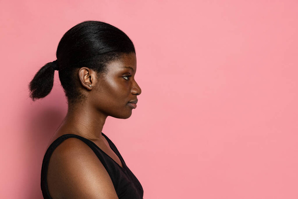 Young beautiful dark skinned woman isolated on pink studio background with copy space for ad. - 写真・画像