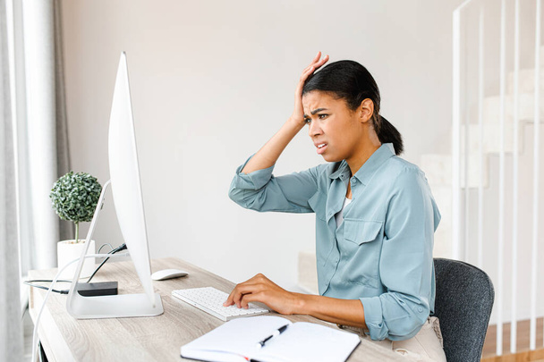 Tired business woman sitting with computer at home and has a problem with remote work. Frustrated woman touching with hand to her head - 写真・画像