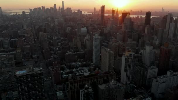 後ろの街の上を飛ぶ。黄金の夕日に対する街並みの空中ビュー。米国ニューヨーク市マンハッタン - 映像、動画
